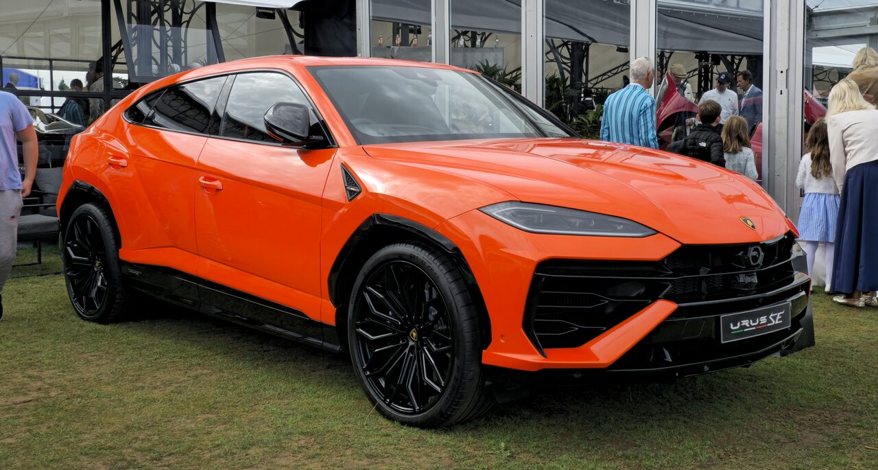 Lamborghini Urus SE laranja exposto sobre a grama, com visitantes ao fundo